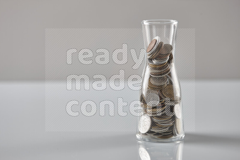 Random old coins in a glass jar on grey background