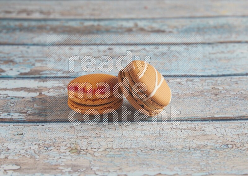 45º Shot of of two assorted Brown Irish Cream, and Orange Exotic macarons on light blue background