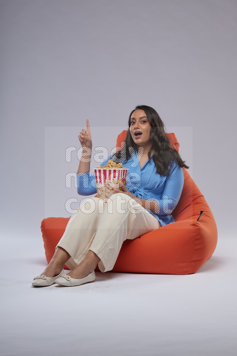 A woman sitting on an orange beanbag and eating popcorn