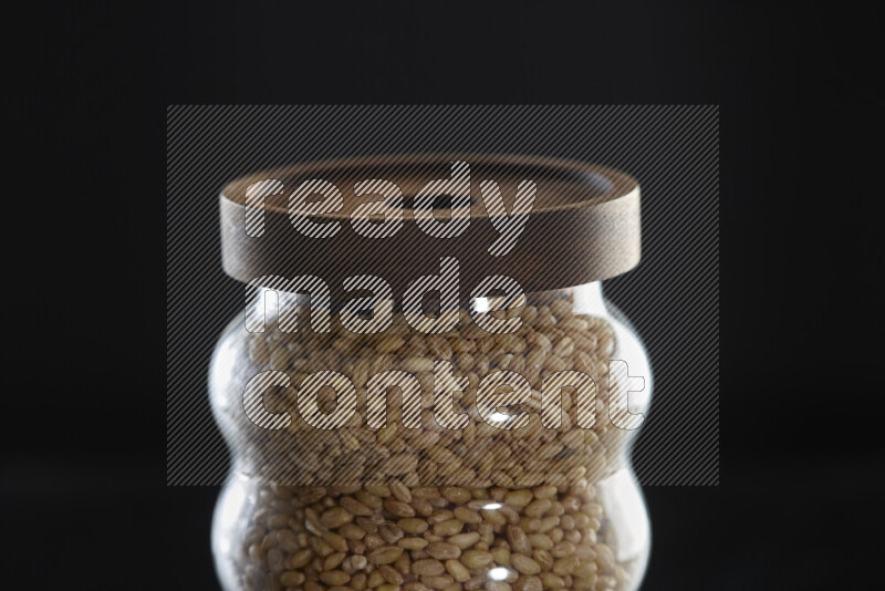 Hulled wheat in a glass jar on black background