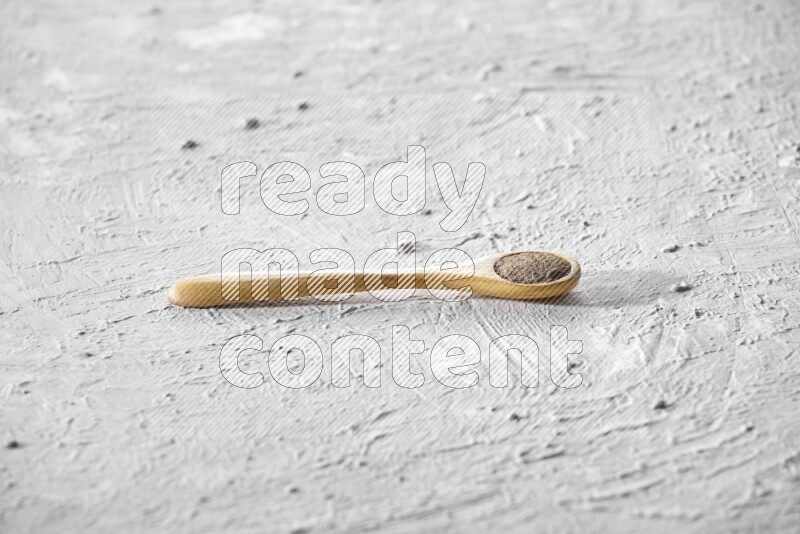 A wooden spoon full of black pepper powder on a textured white flooring