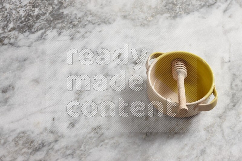 Multicolored pottery bowl with wooden honey dipper in it on grey marble background