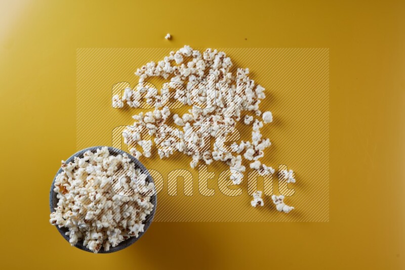 A multicolored pottery bowl full of popcorn with popcorn beside it on a yellow background in different angles