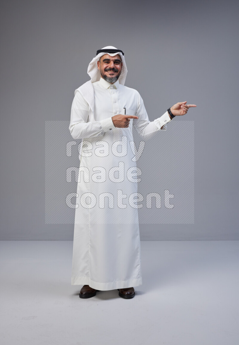 Saudi man Wearing Thob and white Shomag standing interacting with the camera on Gray background