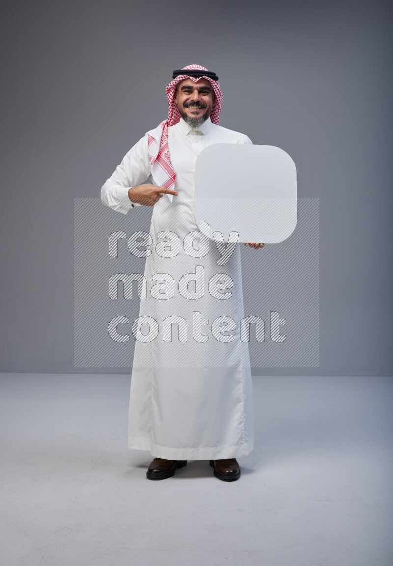 Saudi man Wearing Thob and red Shomag standing holding social media sign on Gray background