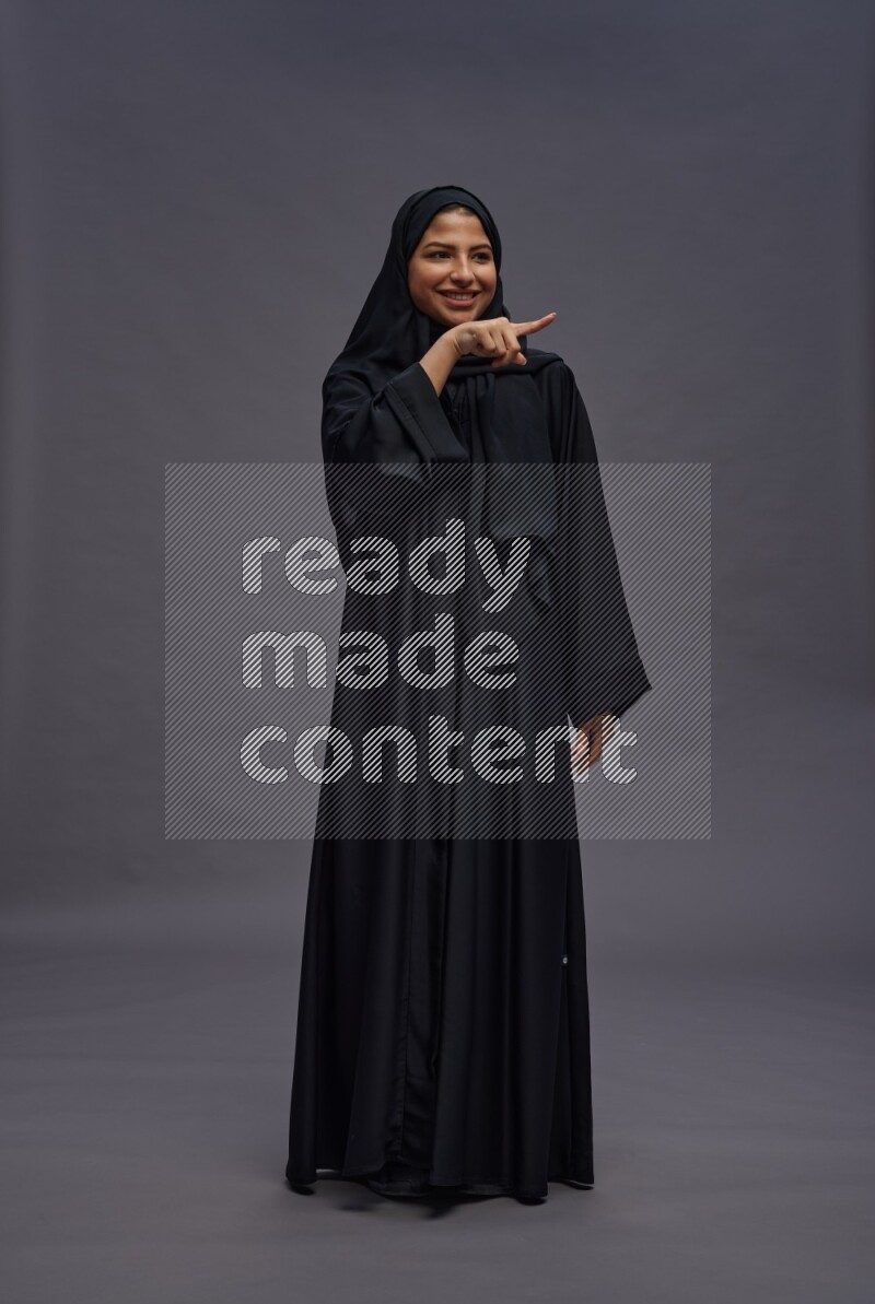 Saudi woman wearing Abaya standing interacting with the camera on gray background