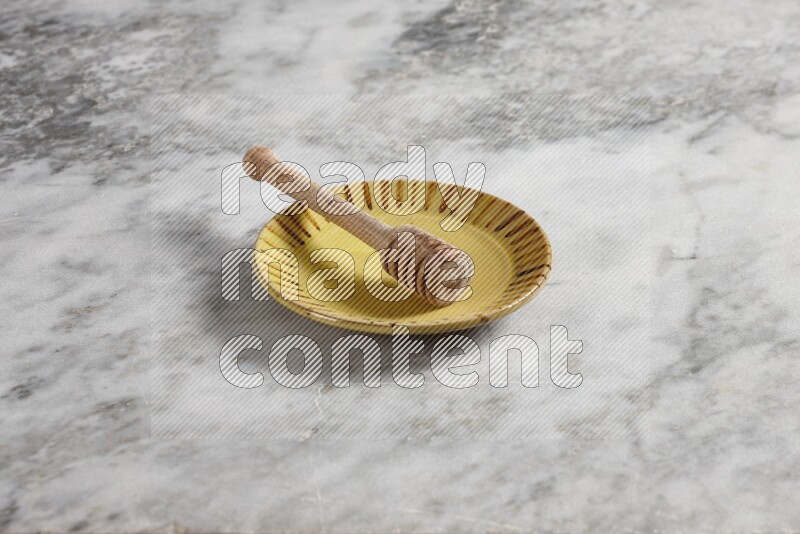 Multicolored pottery plate with wooden honey dipper in it on grey marble background