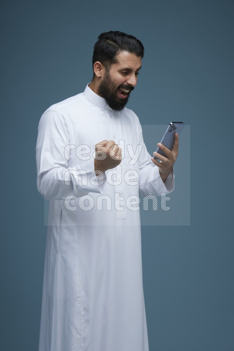 A man Texting in a blue background wearing Saudi Thob