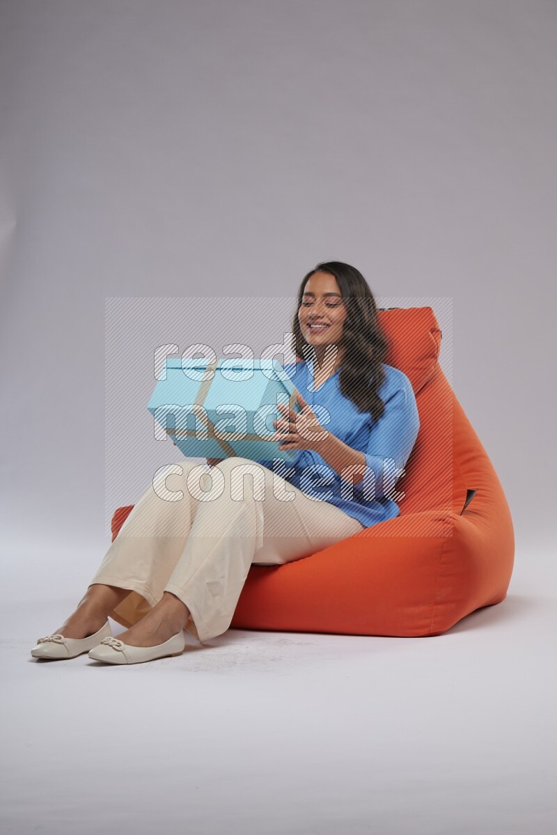 A woman sitting on an orange beanbag and opining a gift