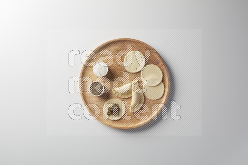 two closed sambosas and one open sambosa filled with meat while salt and black pepper aside in a wooden dish on a white background