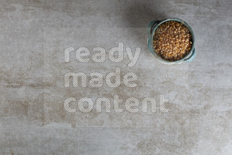 corn kernel in a multi-colored handheld ceramic bowl on a grey textured countertop