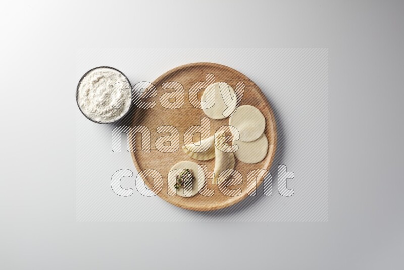 two closed sambosas and one open sambosa filled with meat while flour aside in a wooden dish on a white background