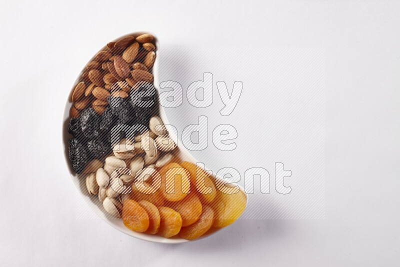 Mixed nuts and dried fruits in a crescent pottery plate on white background