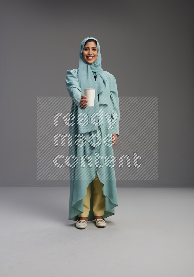 Saudi Woman wearing Abaya standing  holding paper cup on Gray background