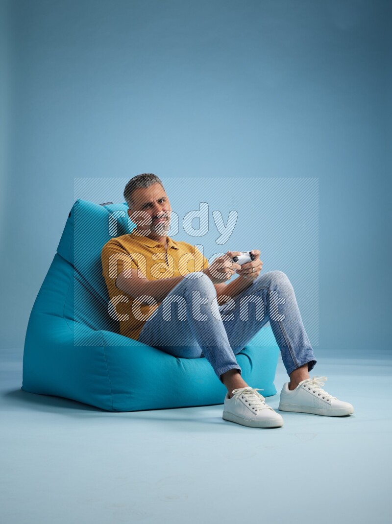 A man sitting on a blue beanbag and gaming with joystick