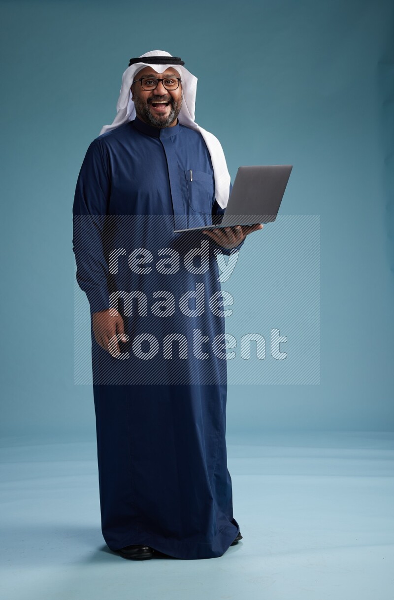Saudi Man with shimag Standing working on laptop on blue background