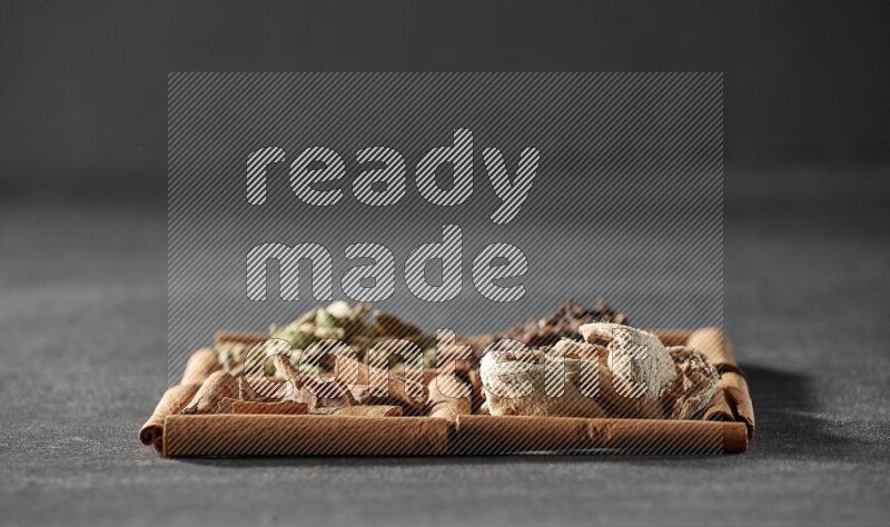 4 squares of cinnamon sticks full of cinnamon, cardamom, cloves and dried ginger on black flooring