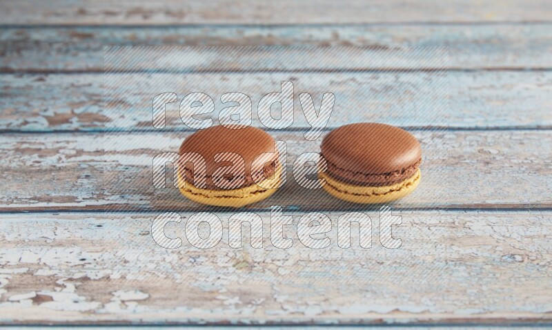 45º Shot of two Yellow and Brown Chai Latte macarons on light blue wooden background