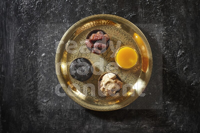 Dried fruits in metal bowls with qamar eldin on a tray in dark setup