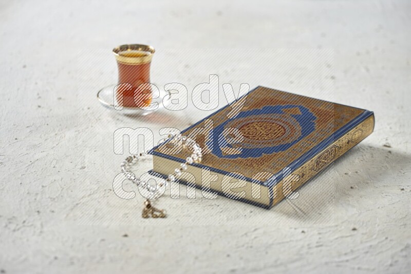 Quran with dates, prayer beads and different drinks all placed on textured white background