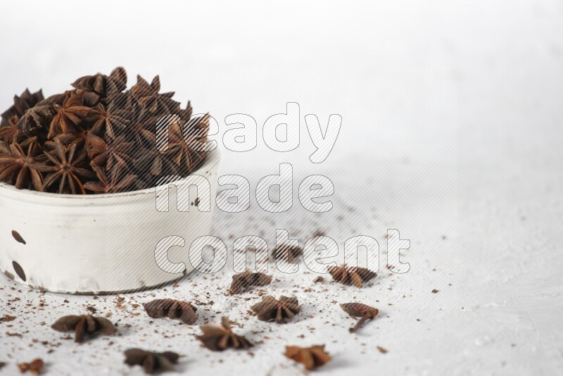 Star Anise in a white bowl and more of it sprinkled on white background