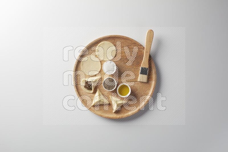 two closed sambosas and one open sambosa filled with meat while salt, black pepper and oil with oil brush aside in a wooden dish on a white background