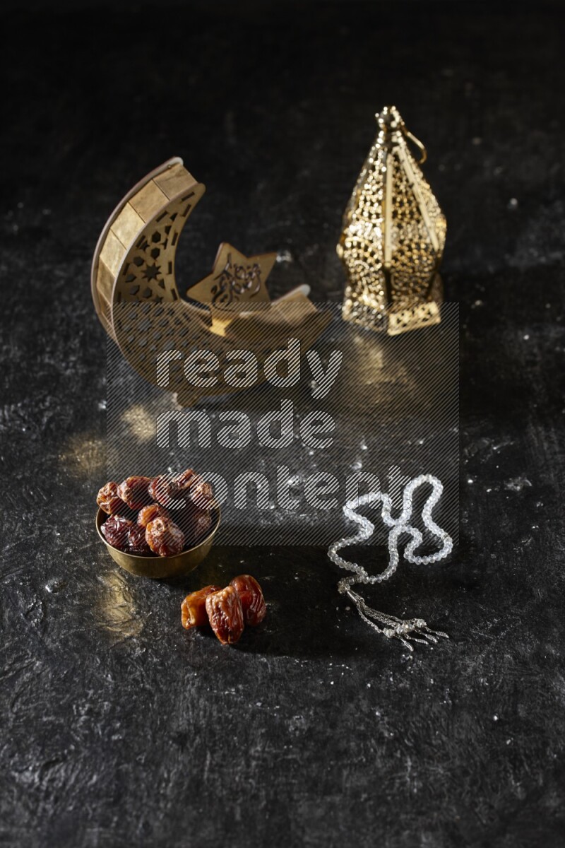 Dates in a metal bowl with prayer beads beside golden lanterns in a dark setup