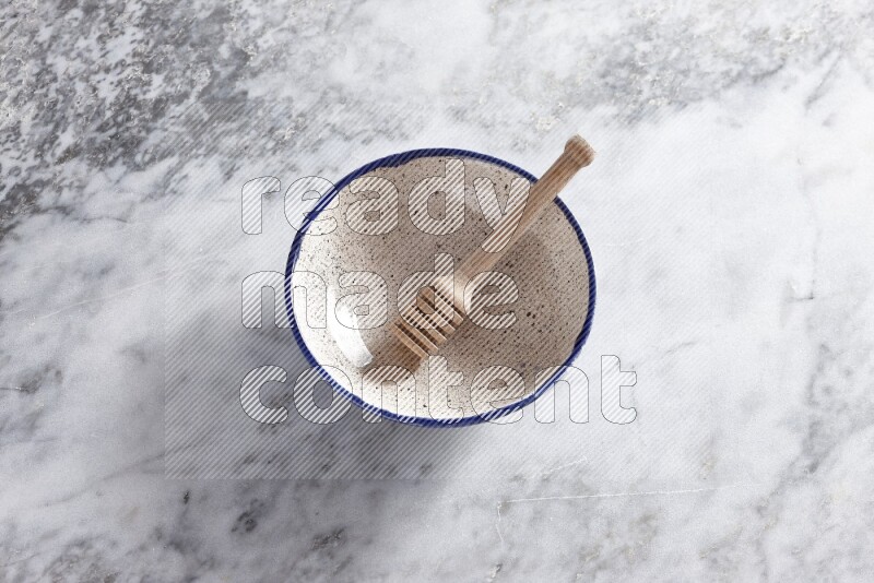 Multicolored pottery bowl with wooden honey dipper in it on grey marble background