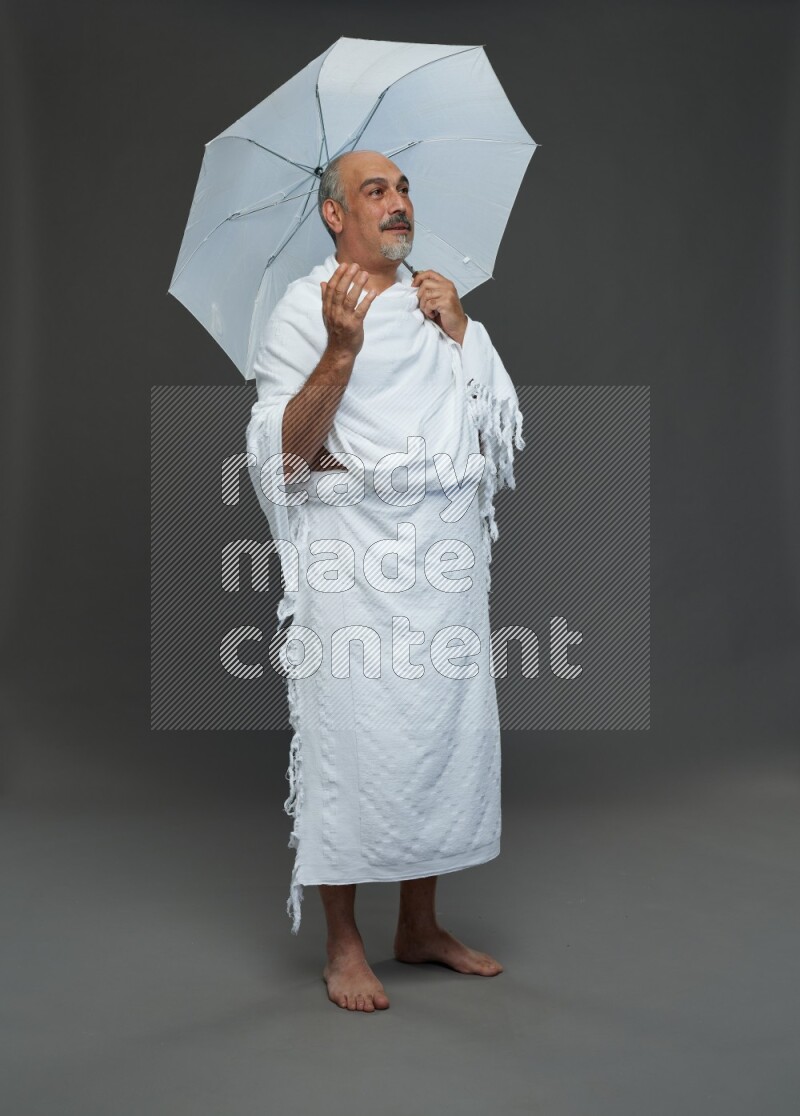 A man wearing Ehram Standing holding umbrella on gray background