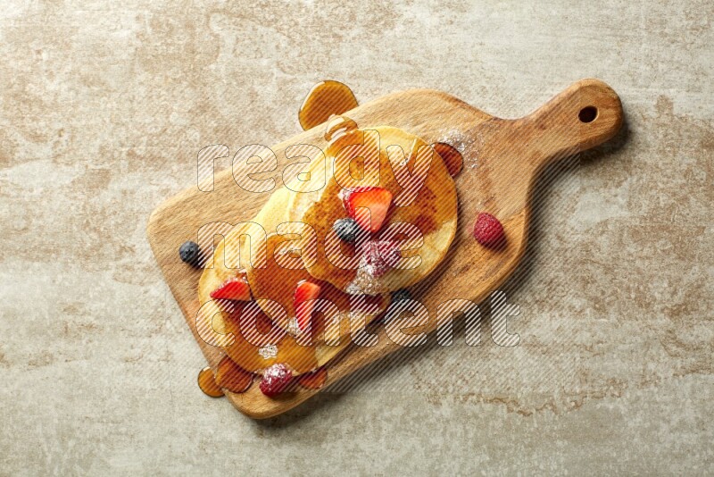 Three stacked mixed berries pancakes on a wooden board on beige background