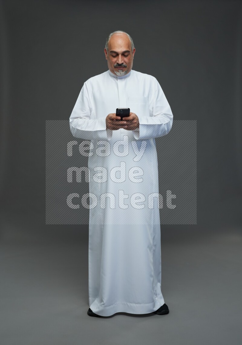 Saudi man without shomag Standing texting on phone on gray background
