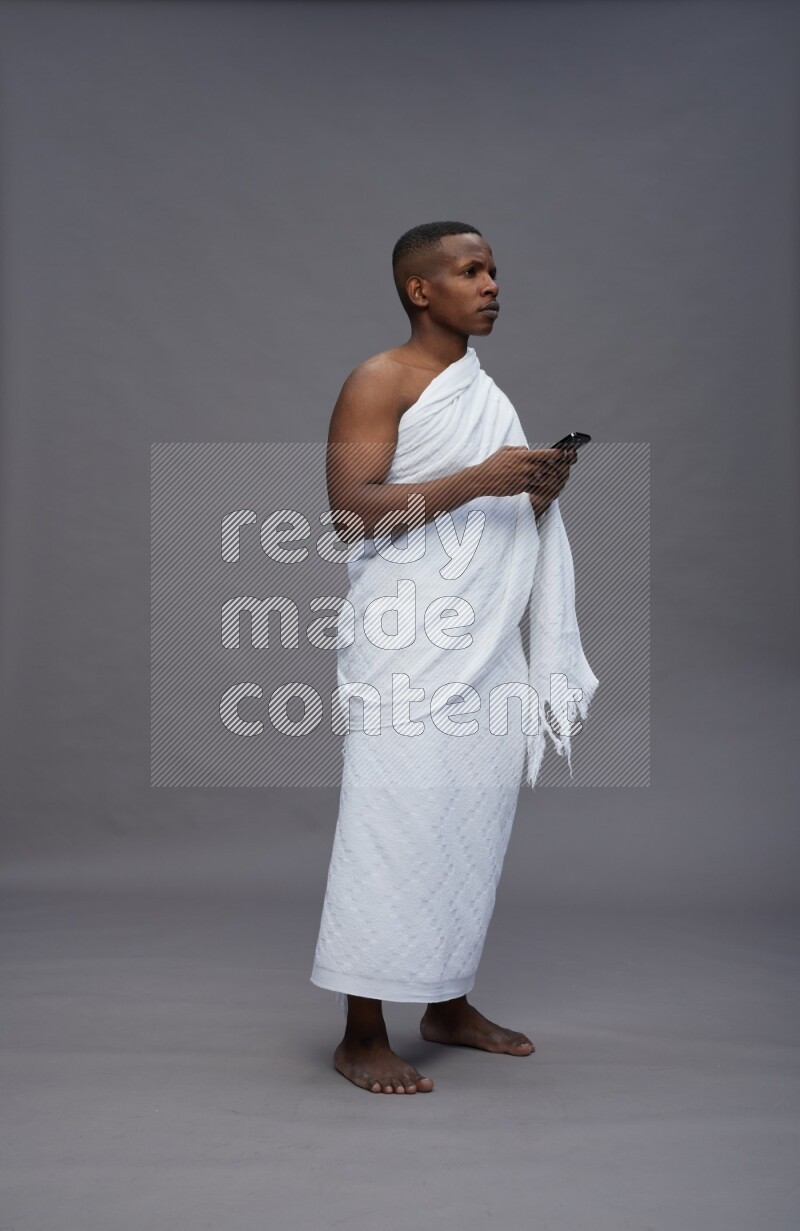 A man wearing Ehram Standing texting on phone on gray background