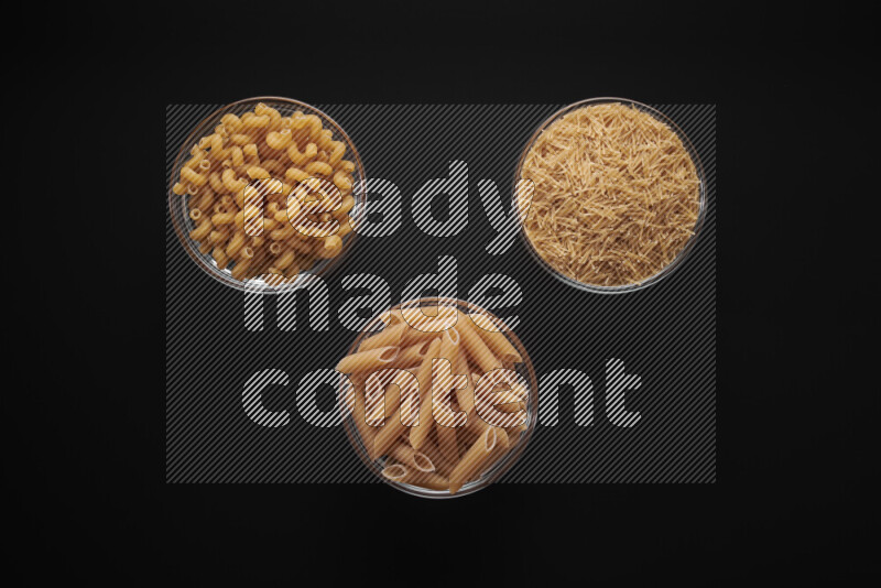 Different pasta types in glass bowls on black background