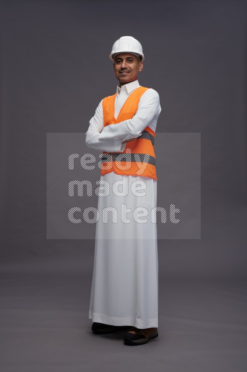 Saudi man wearing thob with engineer vest standing with crossed arms on gray background