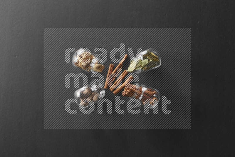 4 glass spice jars full of laurel bay leaves, ginger, cinnamon and nutmeg on black flooring