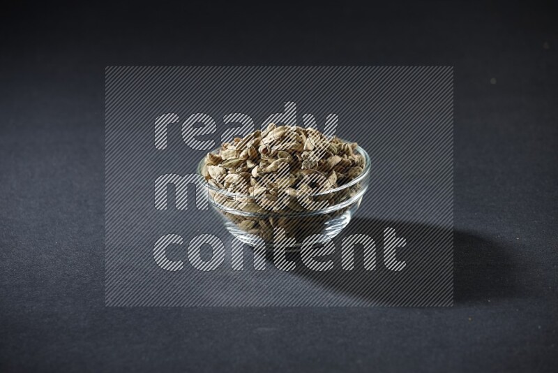 A glass bowl full of cardamom on black flooring