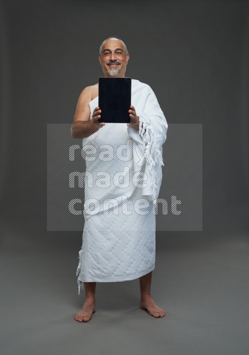 A man wearing Ehram Standing working on tablet on gray background