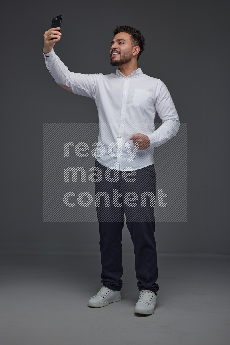 A man wearing smart casual and taking selfie with his phone eye level on a gray background