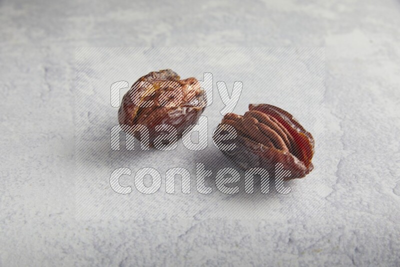 two pecan stuffed madjoul dates on a light grey background