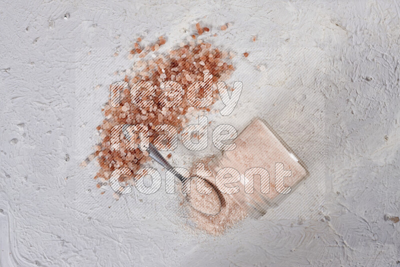 A glass jar full of fine himalayan salt with some himalayan crystals beside it on a white background