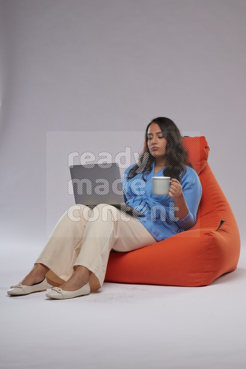 A woman sitting on an orange beanbag and working on laptop