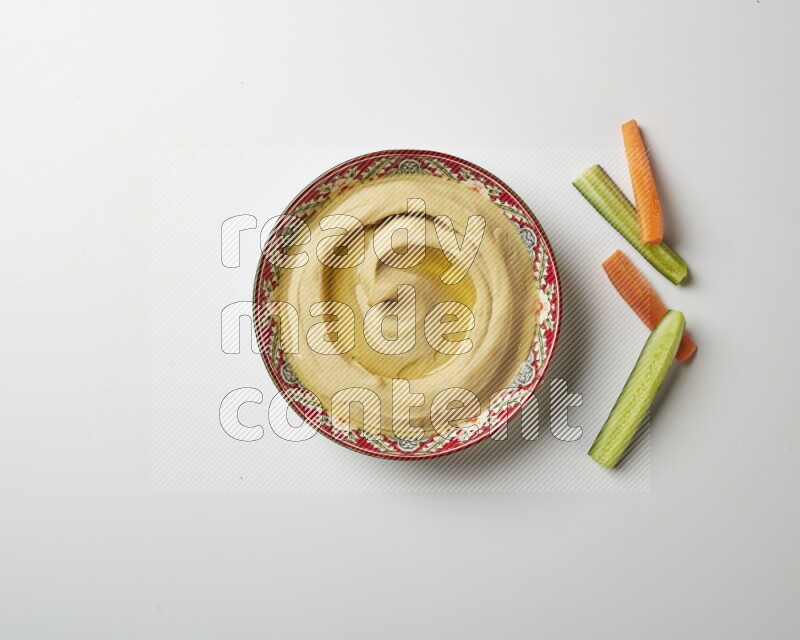 Hummus in a red plate with patterns garnished with olive oil on a white background