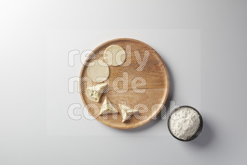 two closed sambosas and one open sambosa filled with cheese while flour aside in a wooden dish on a white background