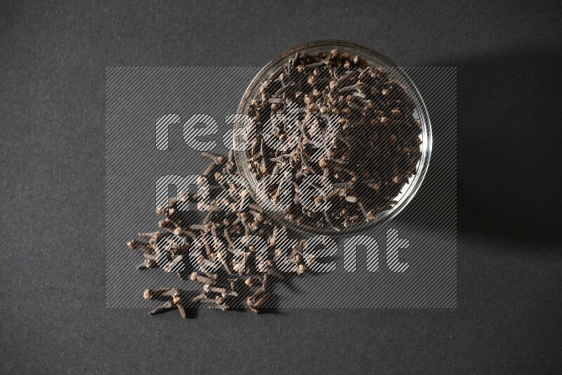 A glass bowl full of cloves on a black flooring