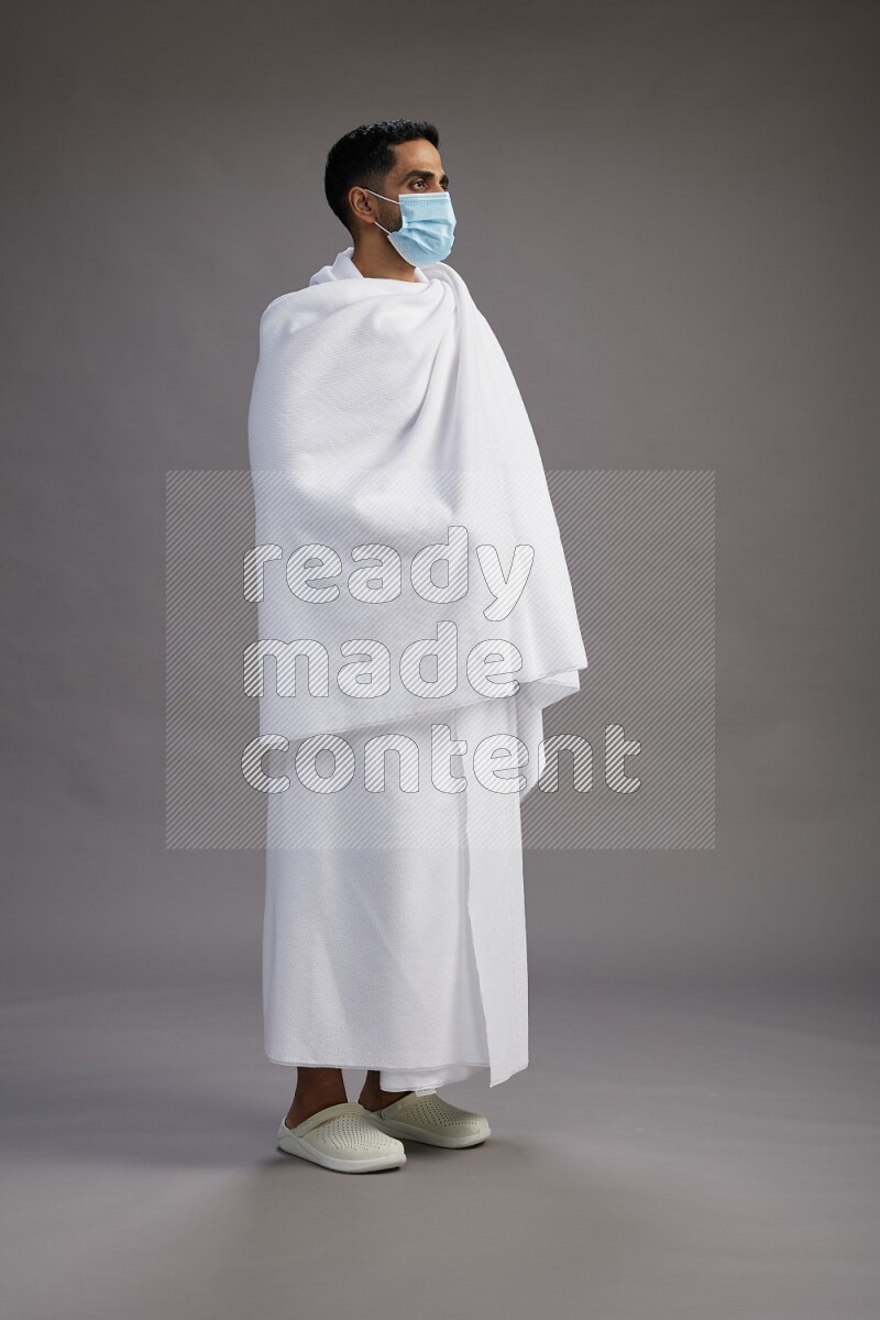 A man wearing Ehram with face mask Standing Interacting with the camera on gray background