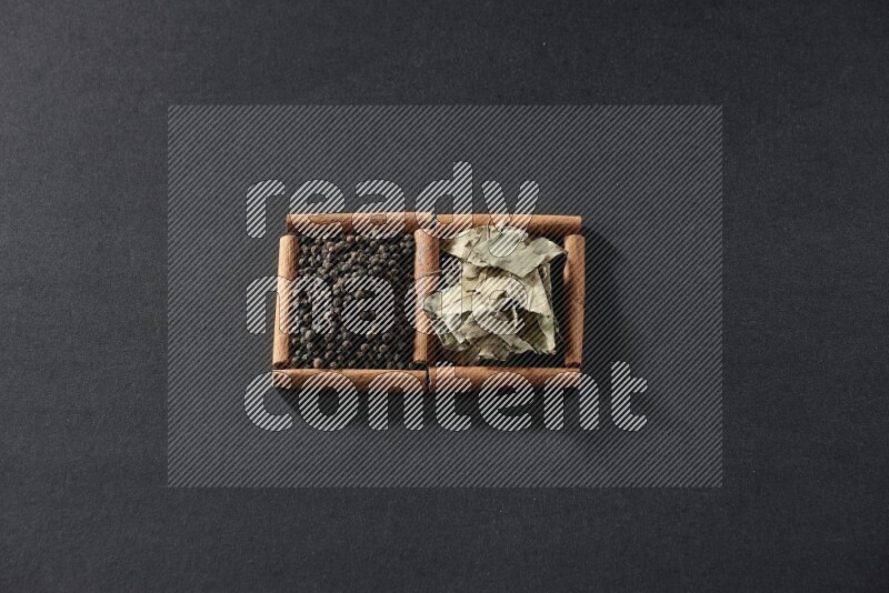 مربعان من أعواد القرفة ممتلئان بحبوب الفلفل الأسود وأوراق الغار علي خلفية سوداء