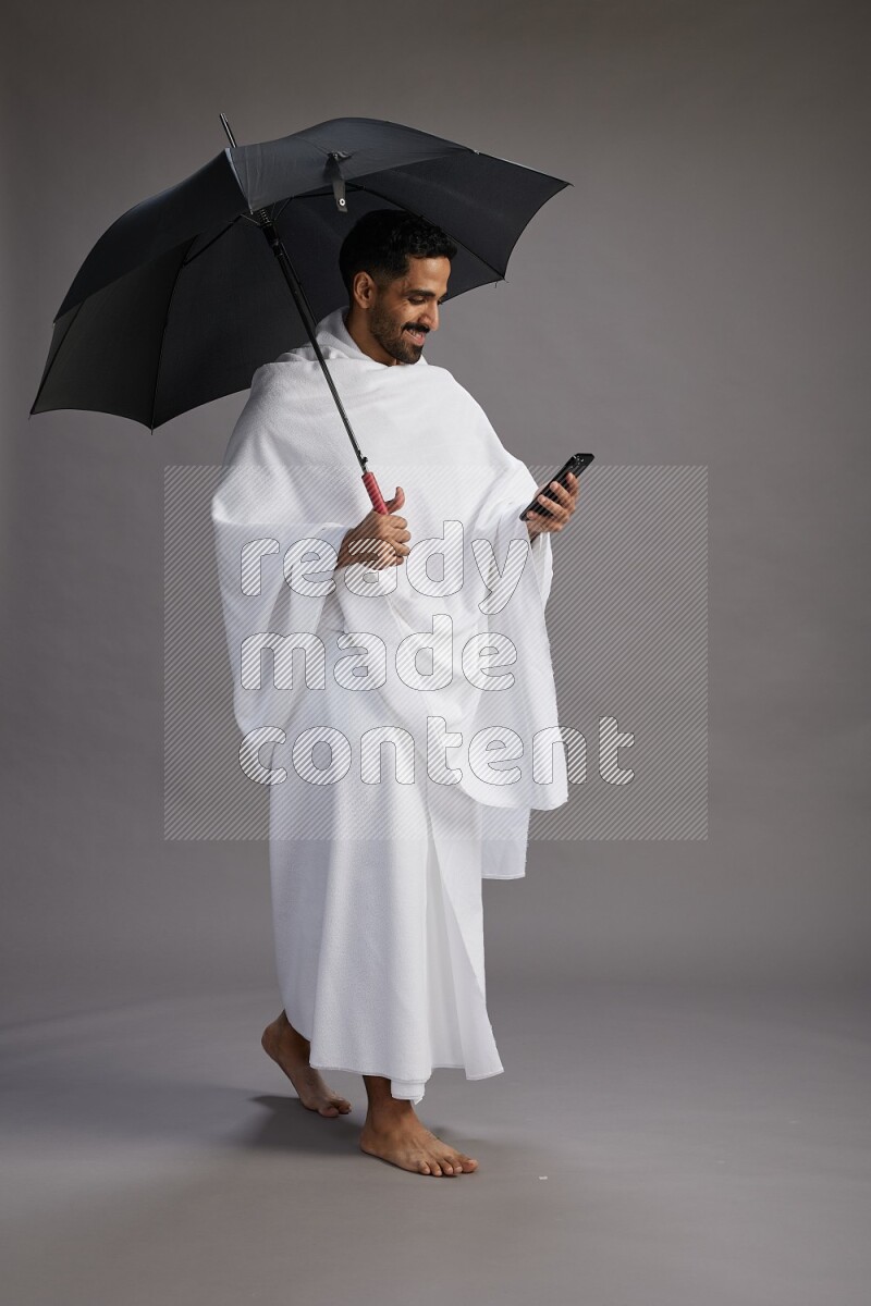 A man wearing Ehram Standing holding umbrella on gray background