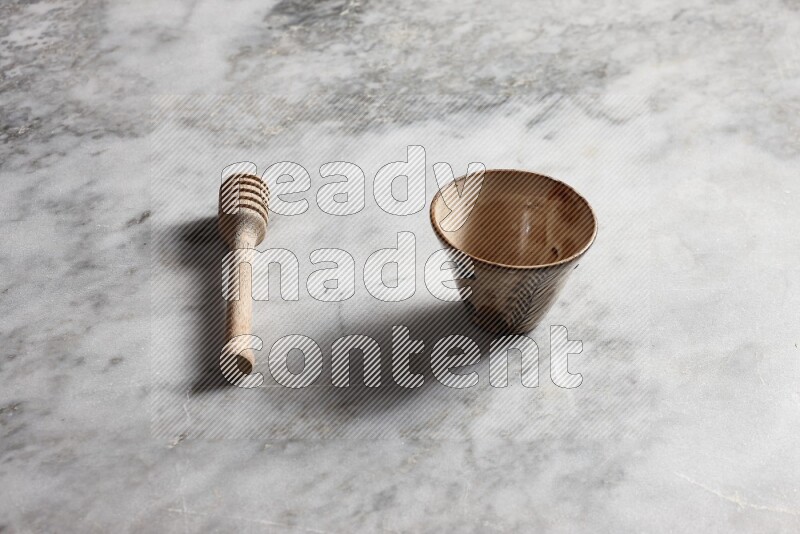 Decorative pottery bowl with wooden honey dipper on the side on grey marble background