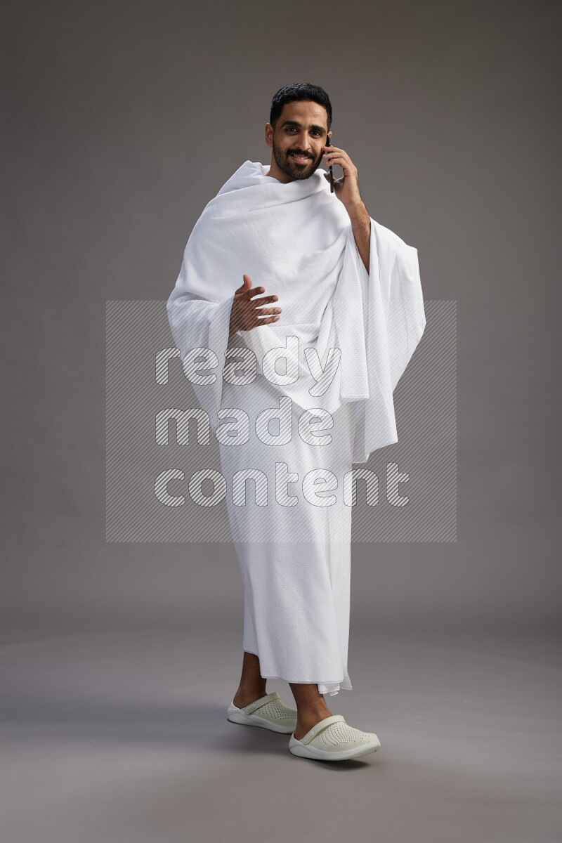 A man wearing Ehram Standing talking on phone on gray background