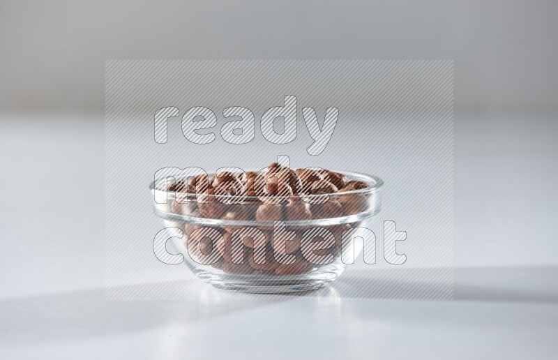 A glass bowl full of peeled hazelnuts on a white background in different angles